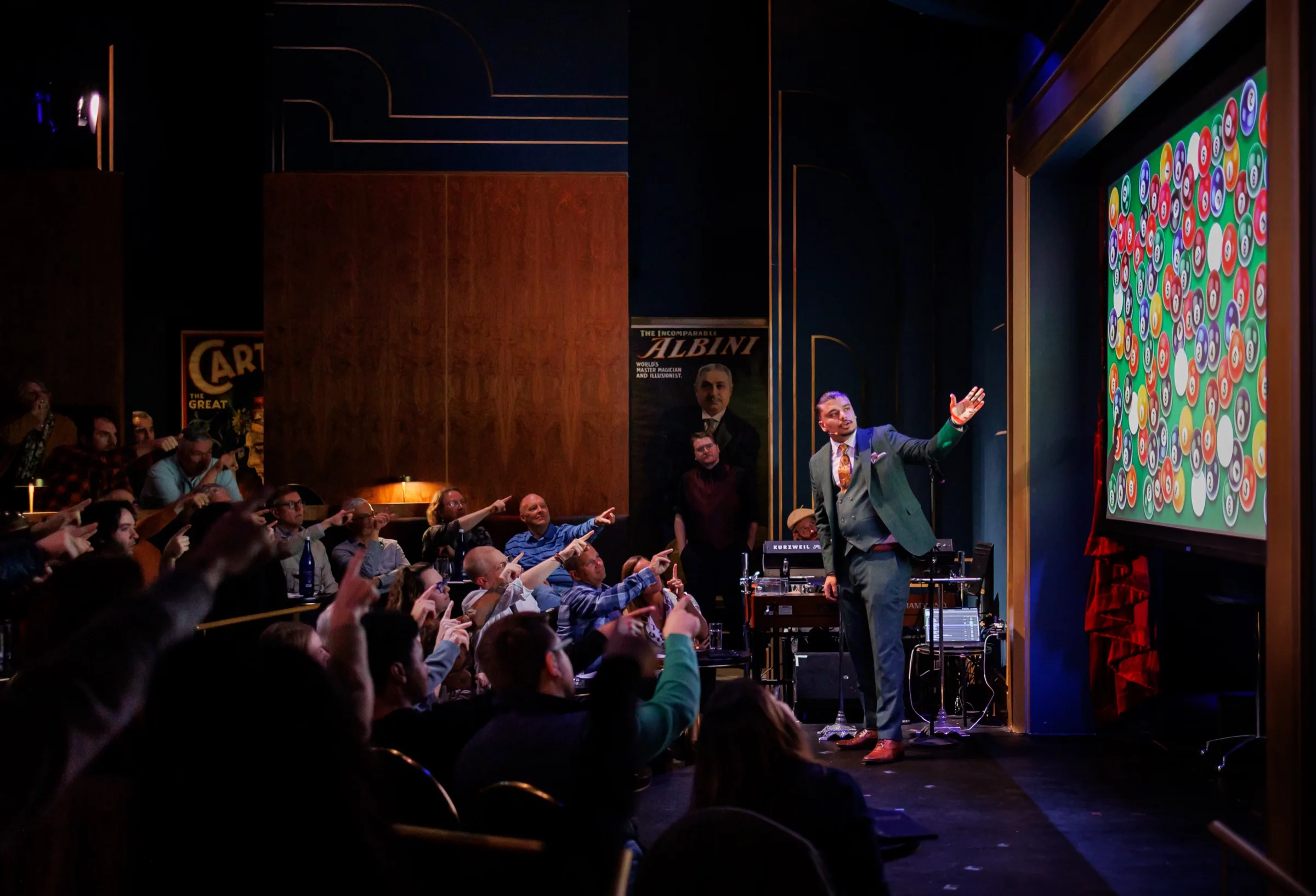 Savio Joseph working a small theatre mid-show, hands raised across the room.